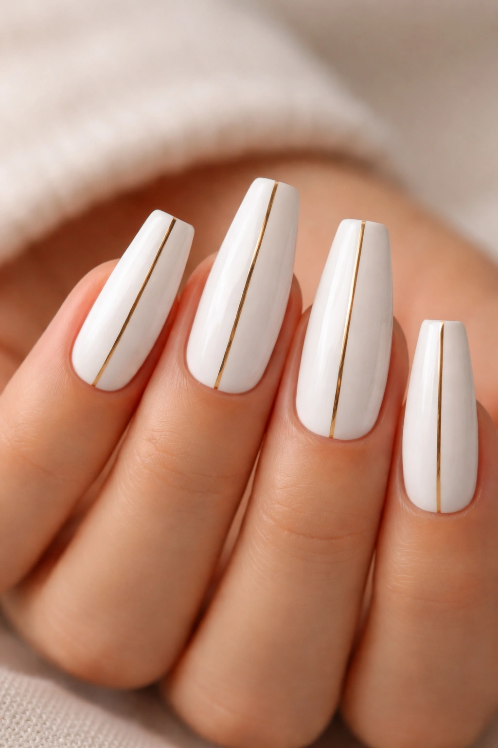 Close-up of white coffin nails with delicate gold stripes