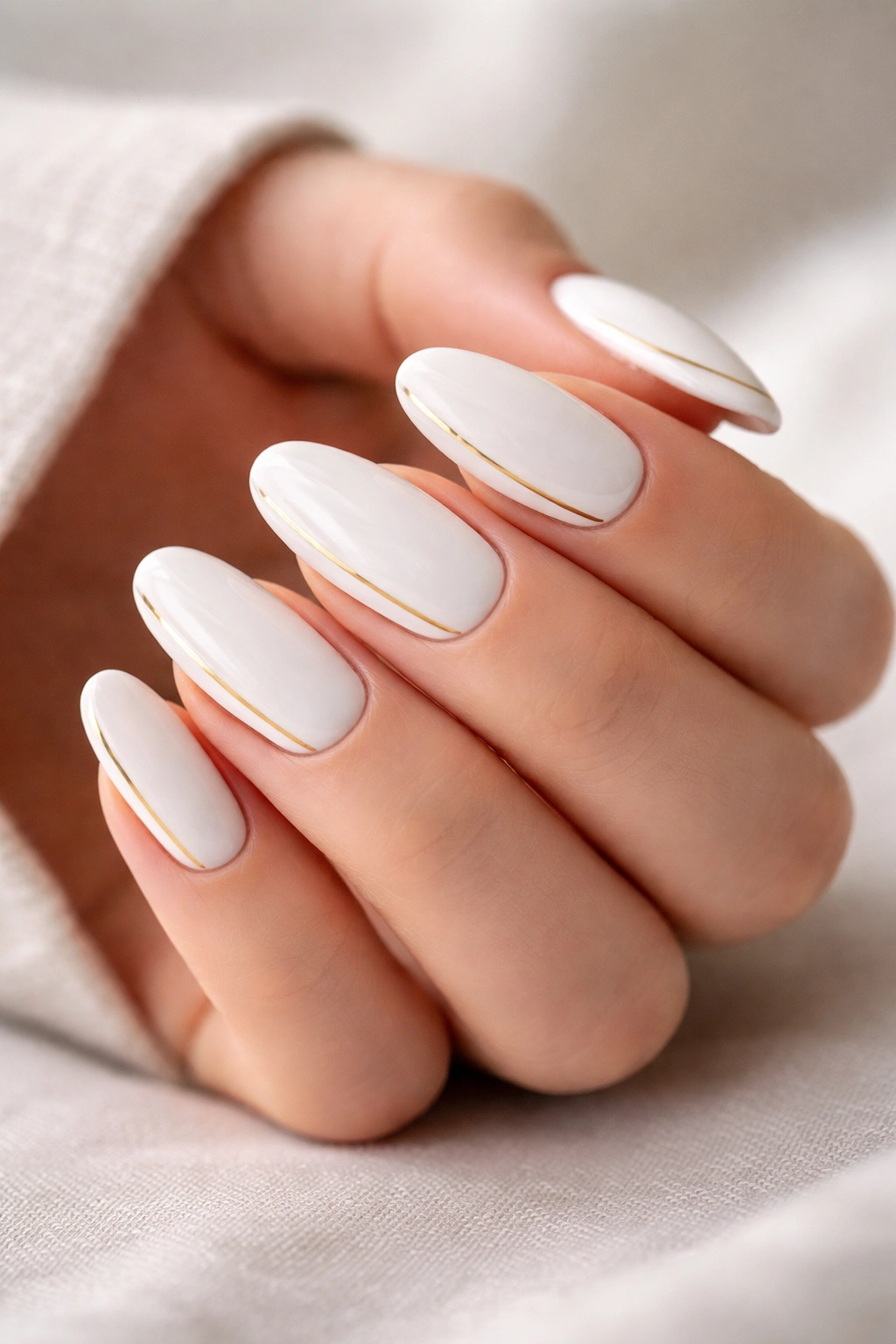 Close-up of pristine white long oval nails with a slim gold line