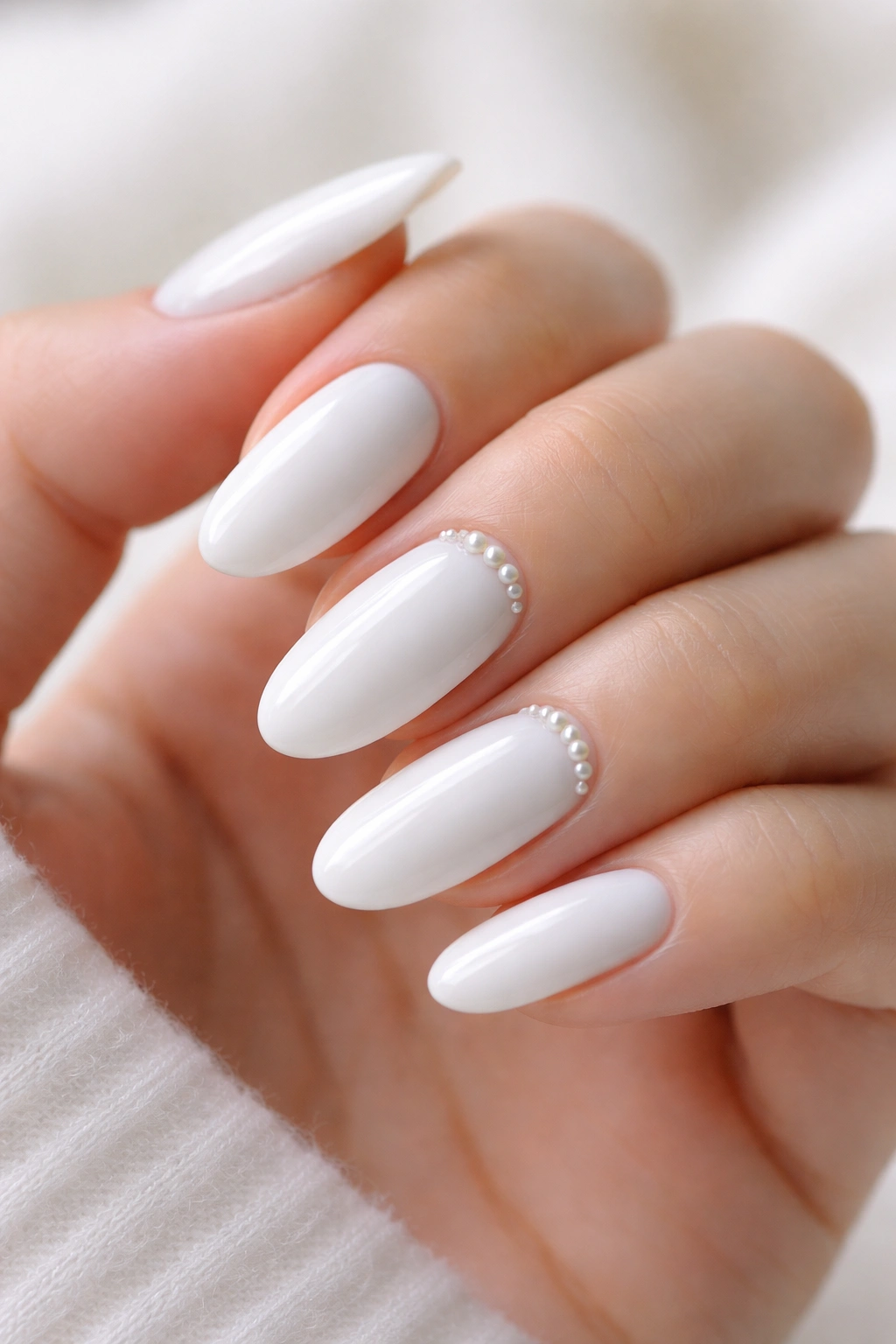 Close-up of white long oval nails with tiny pearl accents near the cuticle