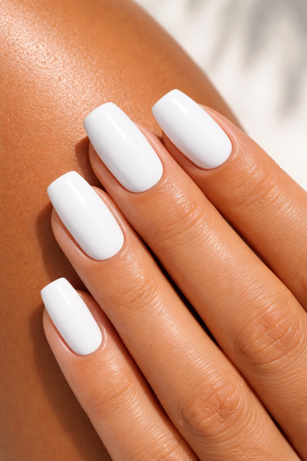 Close-up of nails painted bright white with glossy finish on sun-kissed skin