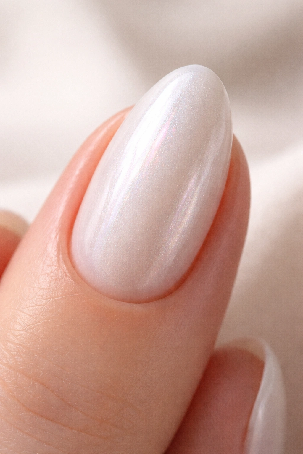 Close-up of a short almond nail in a pearlescent white shade with a soft glow
