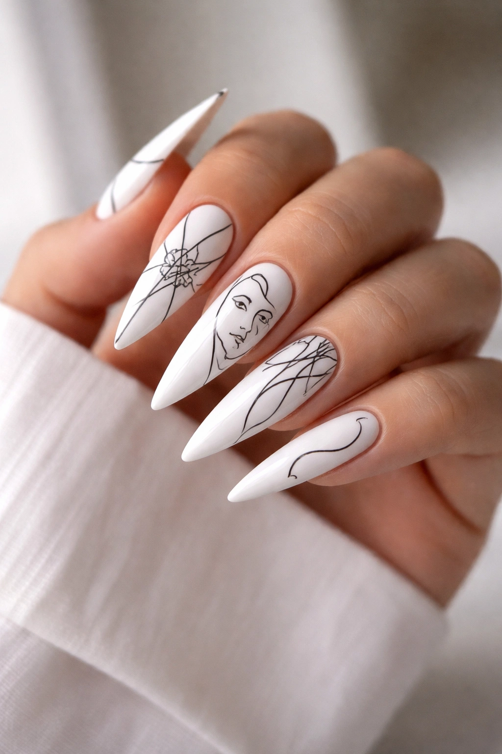 Close-up of white stiletto nails with black line-art designs on each nail