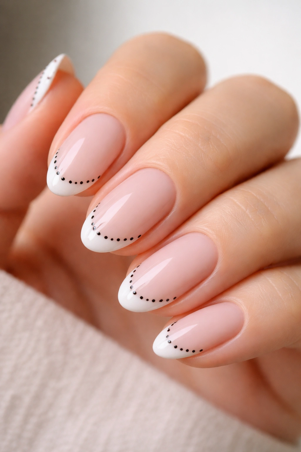 Close-up of short almond nails with white tips and black dot borders