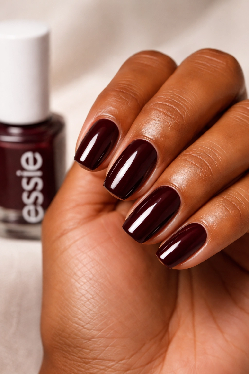 Close-up of nails painted Wicked deep burgundy on medium to deep skin tone