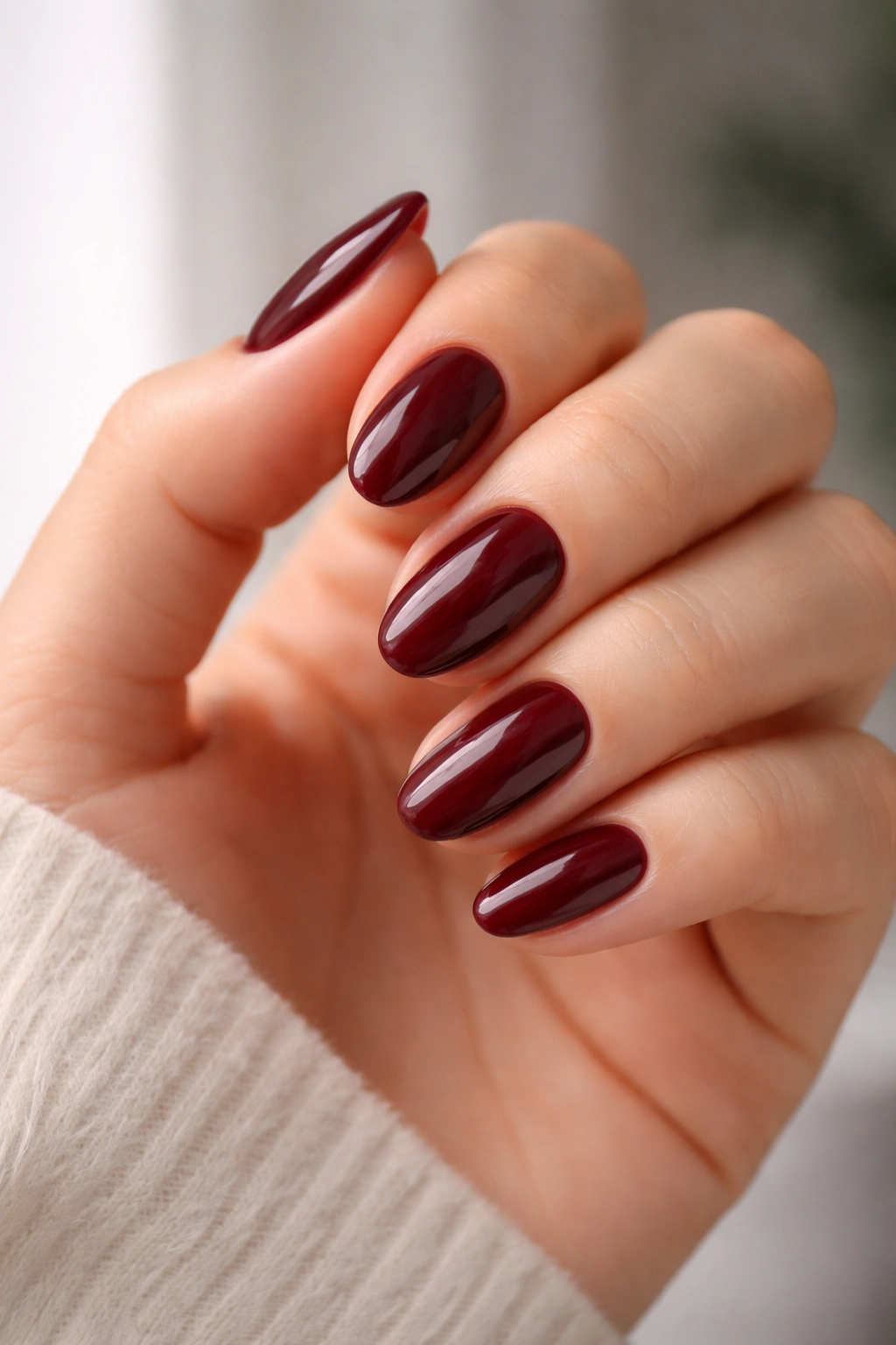 Hand with deep wine red nails and glossy top coat for long wear