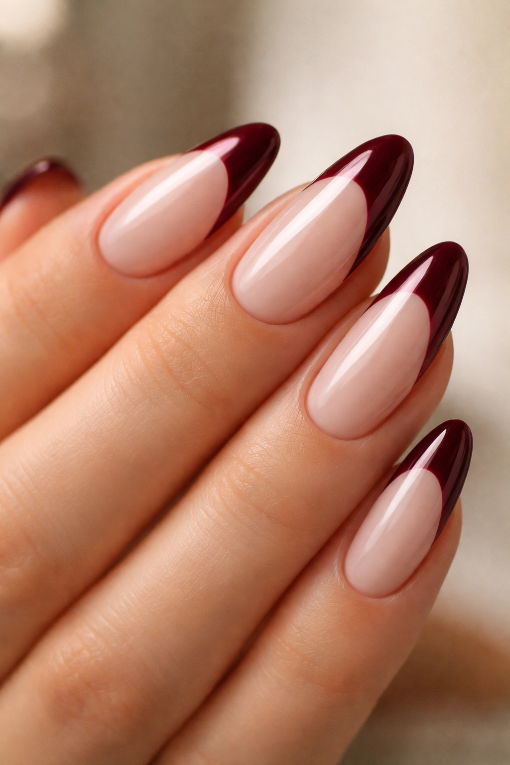 Close-up of almond nails with deep wine tips and milky base.