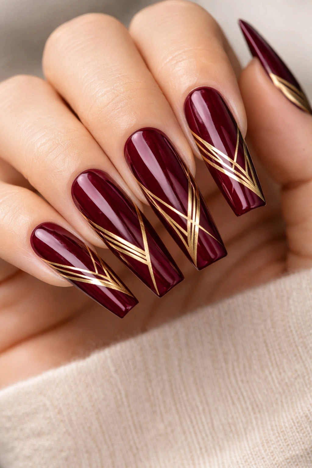 Close-up of coffin nails with deep wine red base and metallic gold geometric shapes