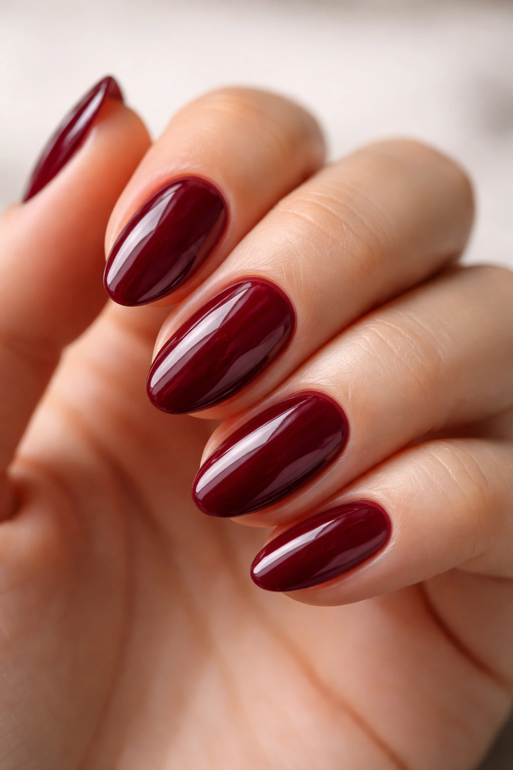 Close-up of short almond nails painted in glossy wine red with high shine