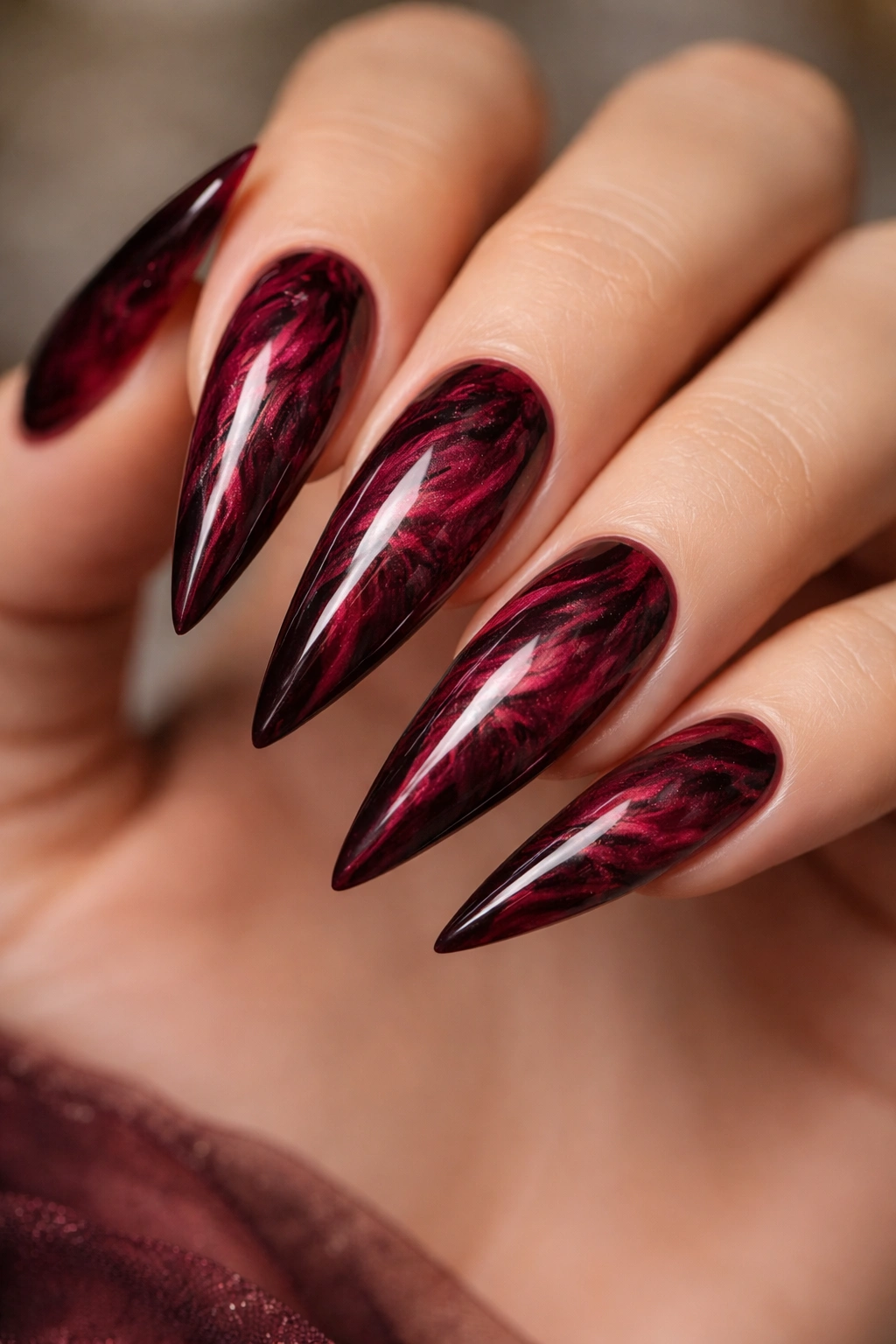 Stiletto nails with burgundy marble swirl on deep wine red base