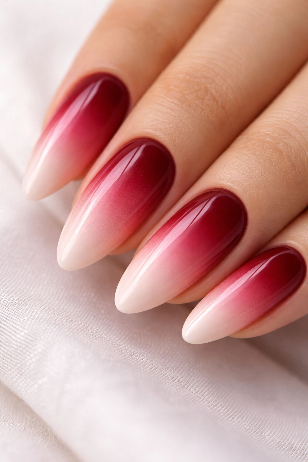 Macro close-up of almond nails with wine red to blush pink ombre on a white background