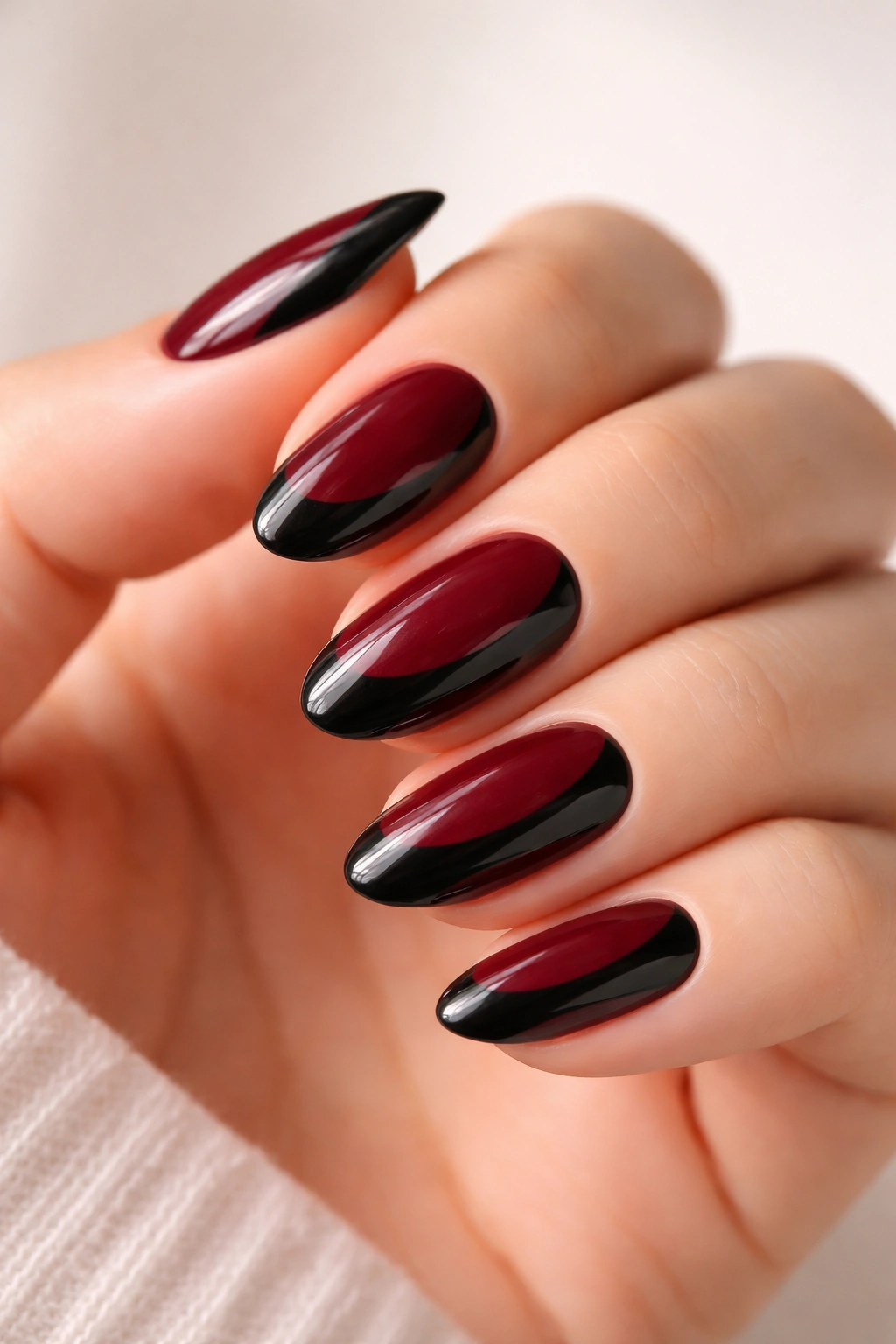 Close-up of short almond nails with black and wine red side-French design on a neutral background