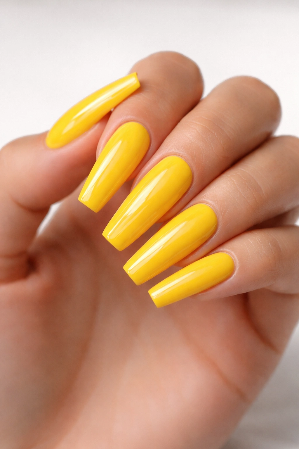 Close-up of long coffin nails in bright sunshine yellow with a glossy finish.