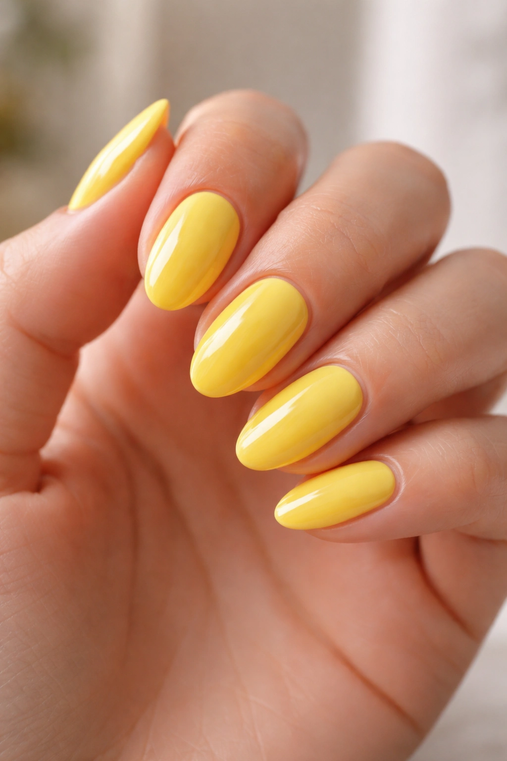 Hand with short almond yellow nails showing glossy finish and clean cuticles