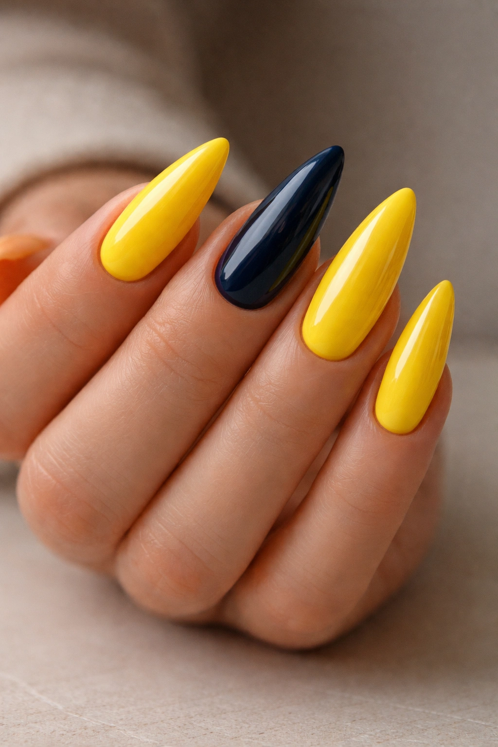 Hand displaying five yellow stiletto nails with a navy accent nail on the middle finger