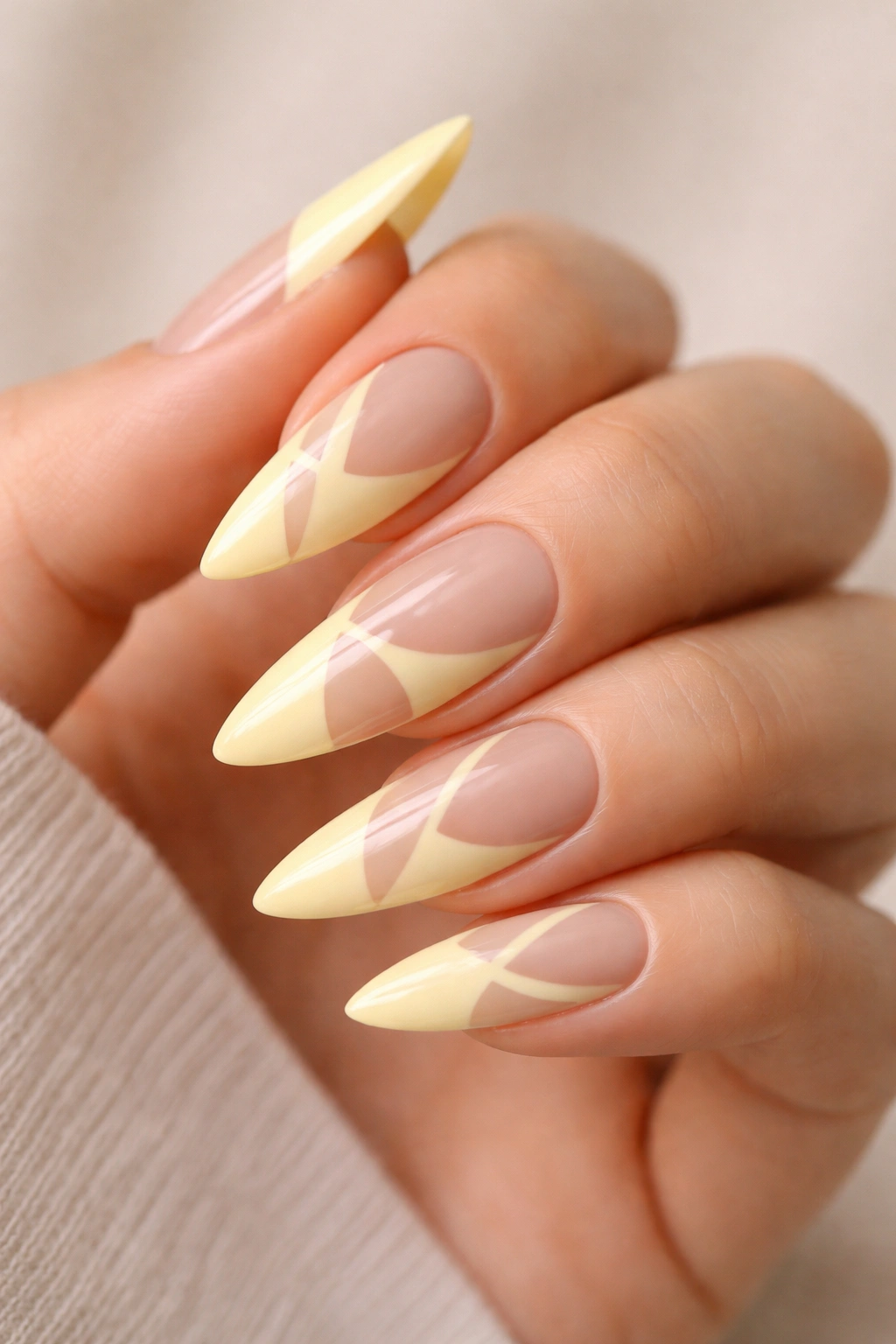 Close-up of pale yellow stiletto nails with negative space designs on a clean background