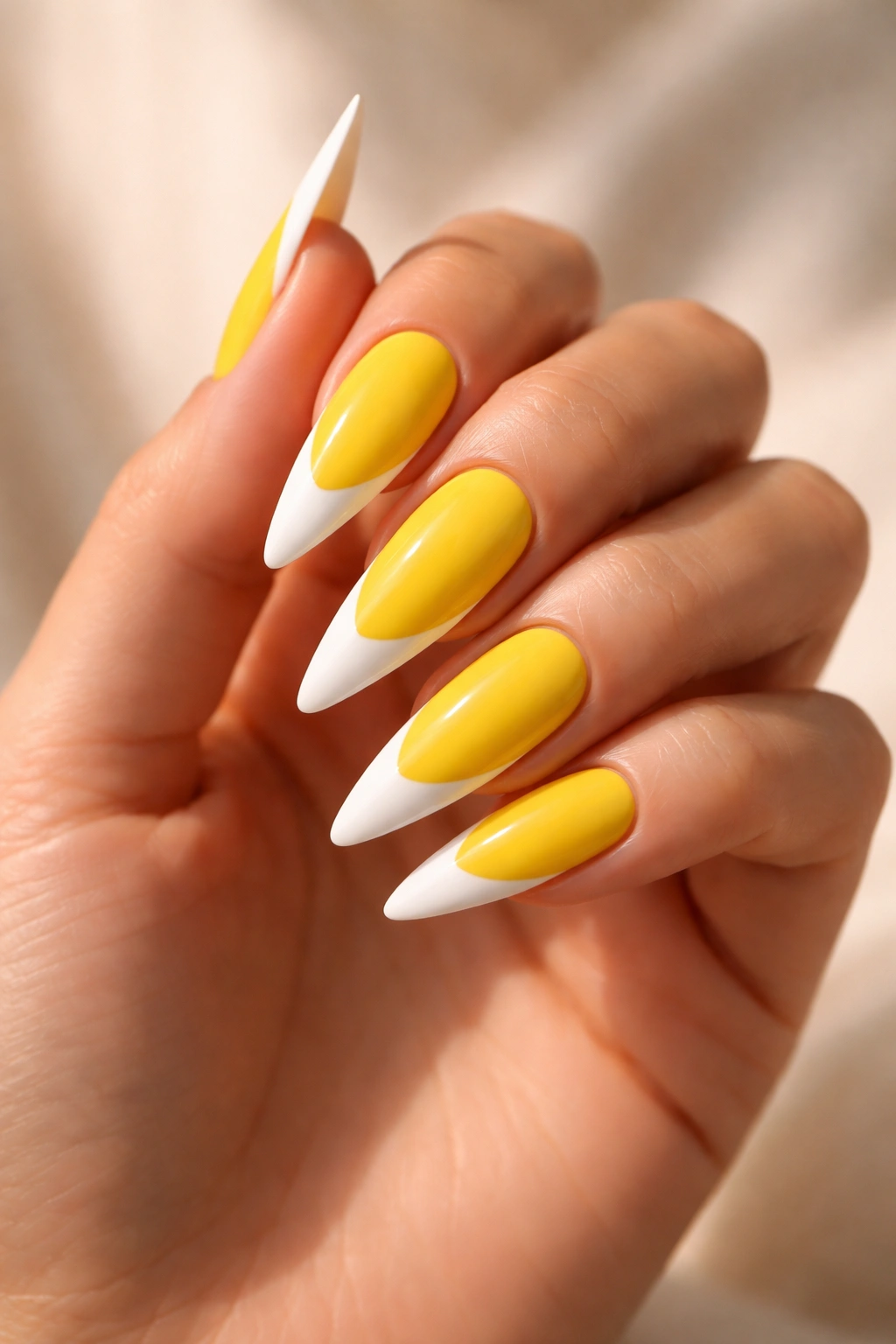 Close-up of five yellow stiletto nails with white French tips on a hand