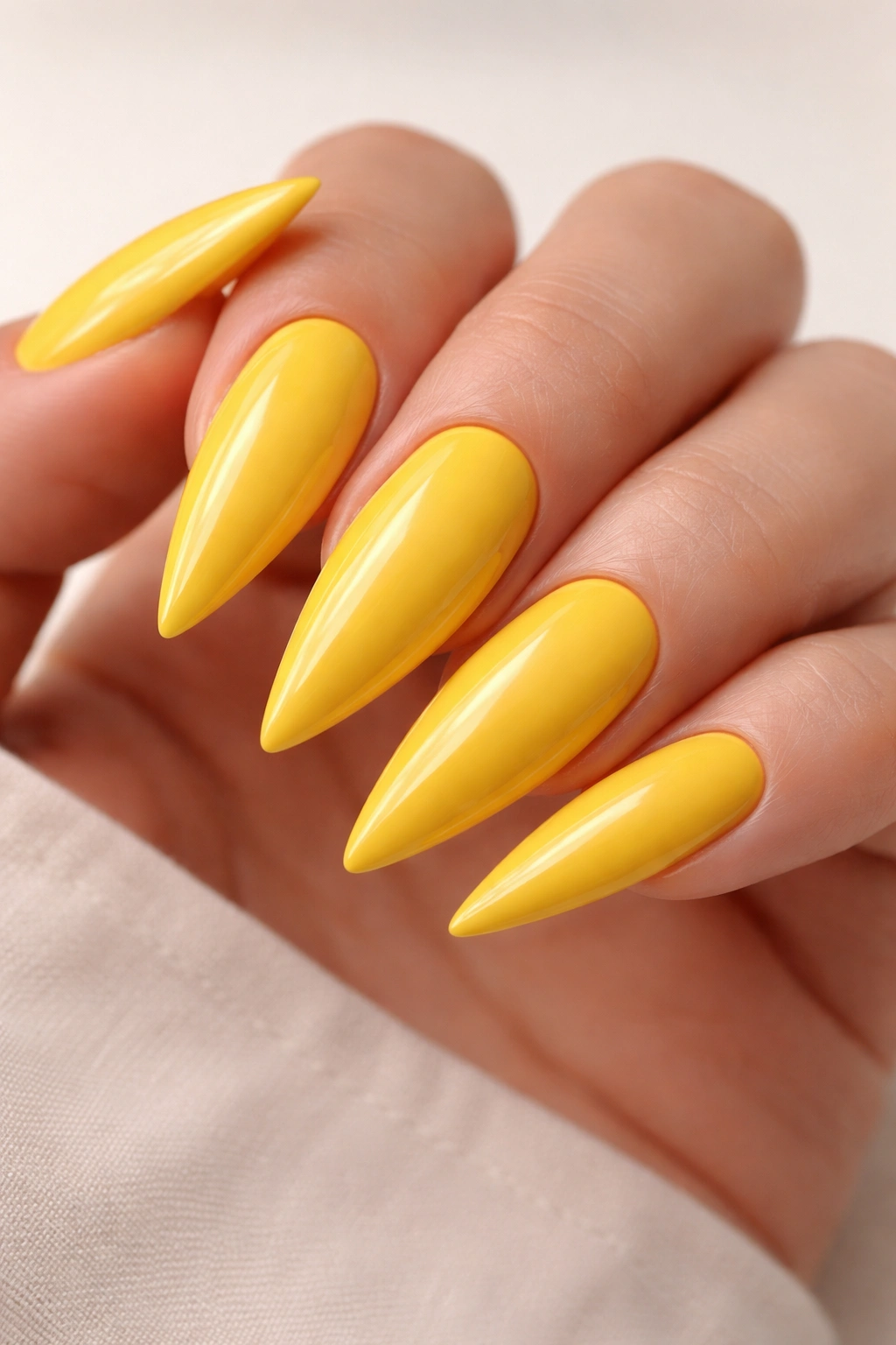 Close-up of five glossy yellow stiletto nails on a neutral background
