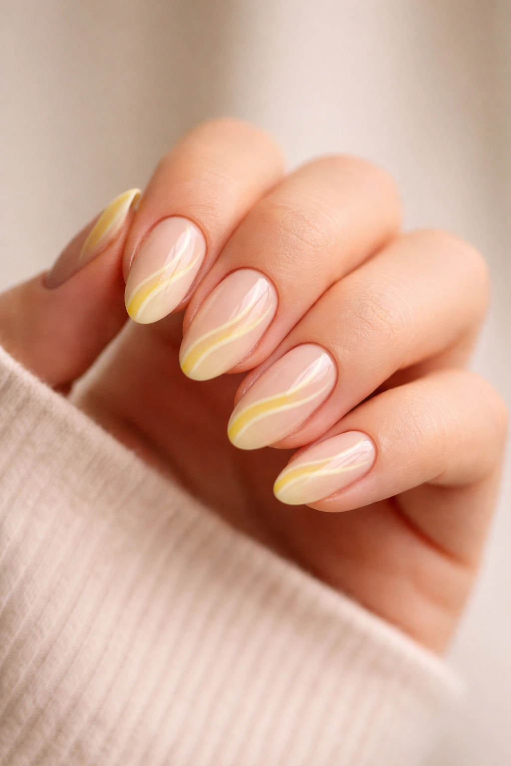 Close-up of short almond nails with yellow swirls on nude base