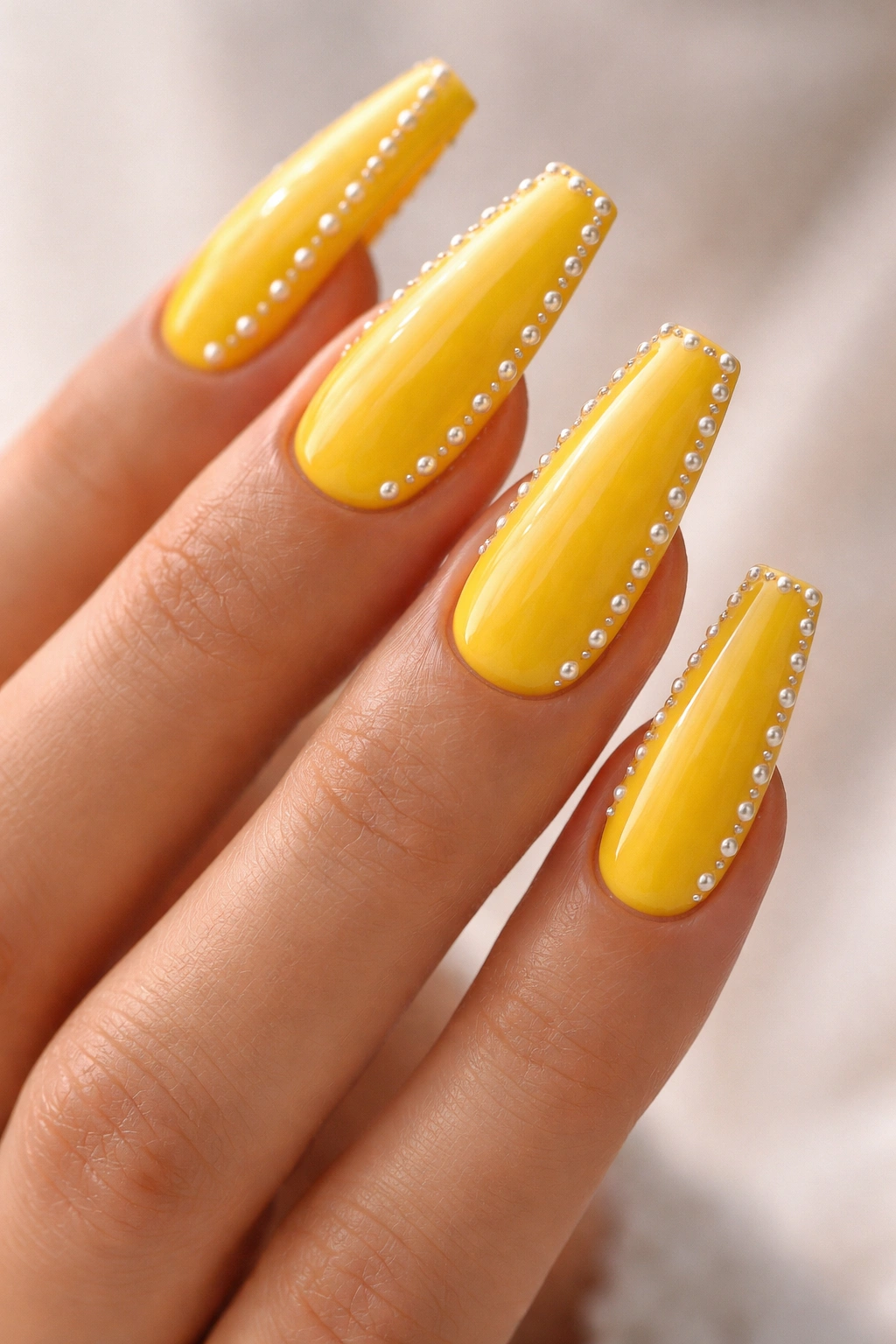 Bright yellow coffin nails with small pearl studs along the edge