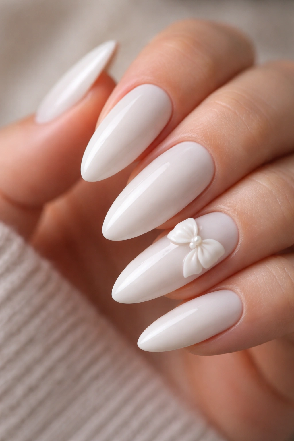 Close-up of a milky white almond nail with a small 3D gel bow on an accent nail