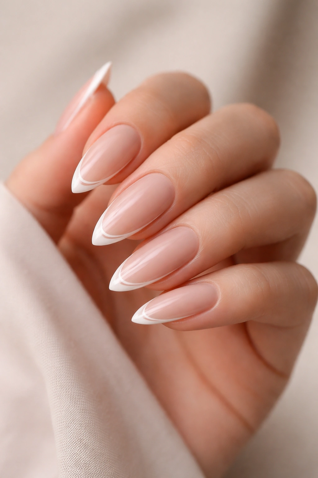 Close-up of long almond nails with a hairline-thin white French tip on a nude base