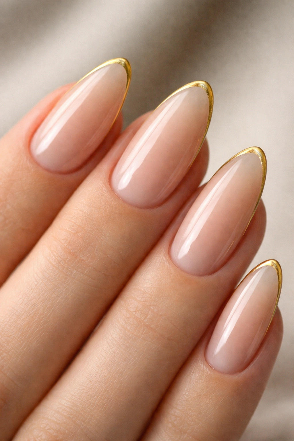 Close-up of sheer nude almond nails with a hairline gold smile line