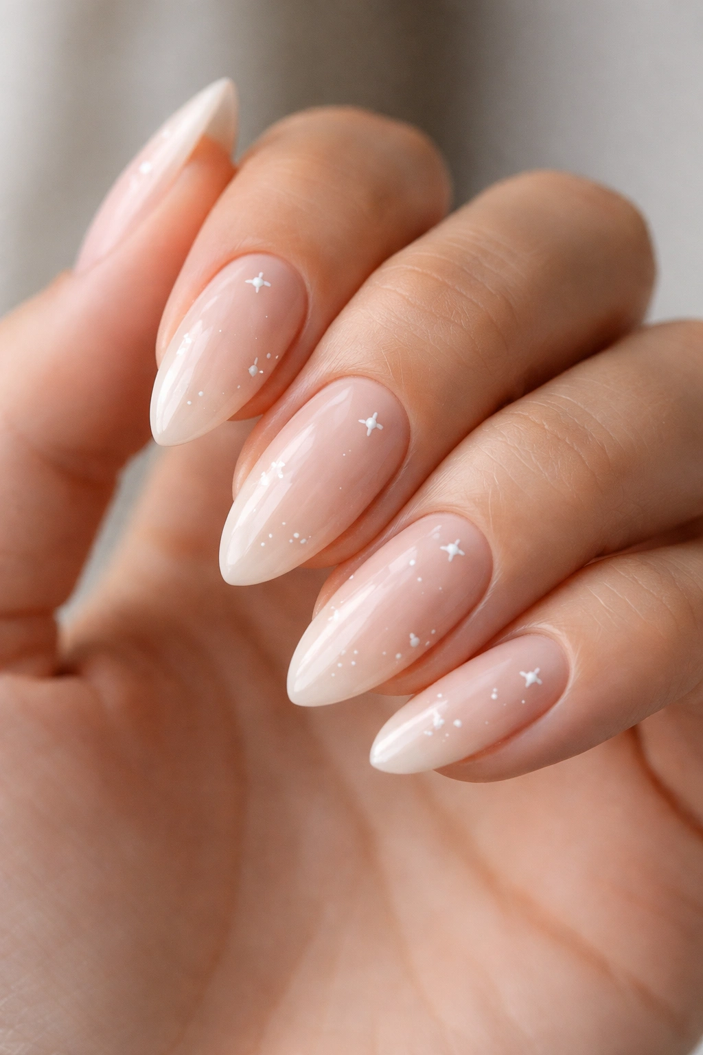 Close-up of almond nails with a sheer nude base and tiny white stars