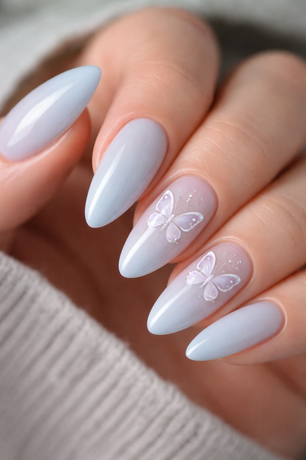 Close-up of almond nails with baby blue base and tiny butterfly decals.