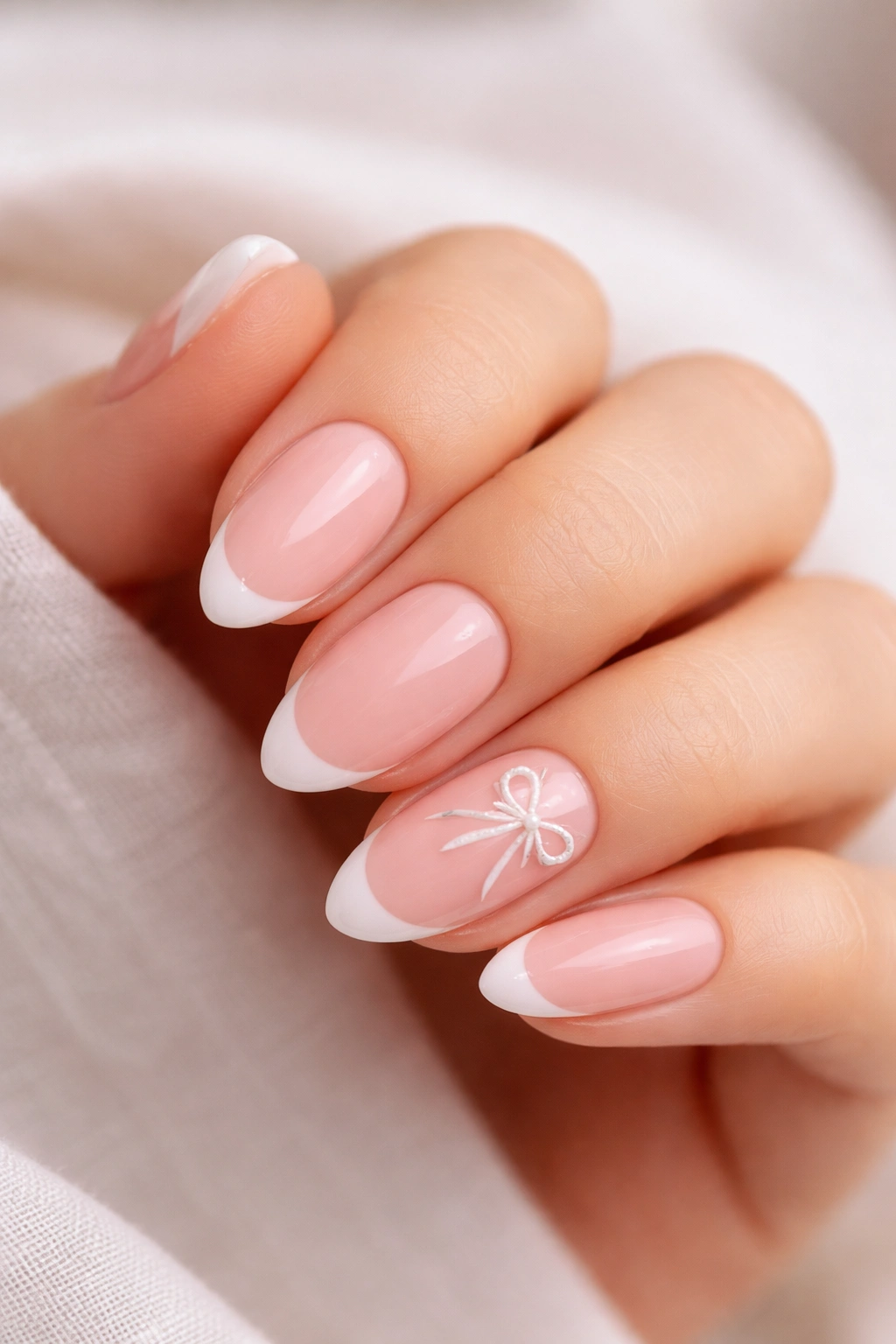 Almond nails with ballet pink base and delicate ribbon-line bow on accent nail
