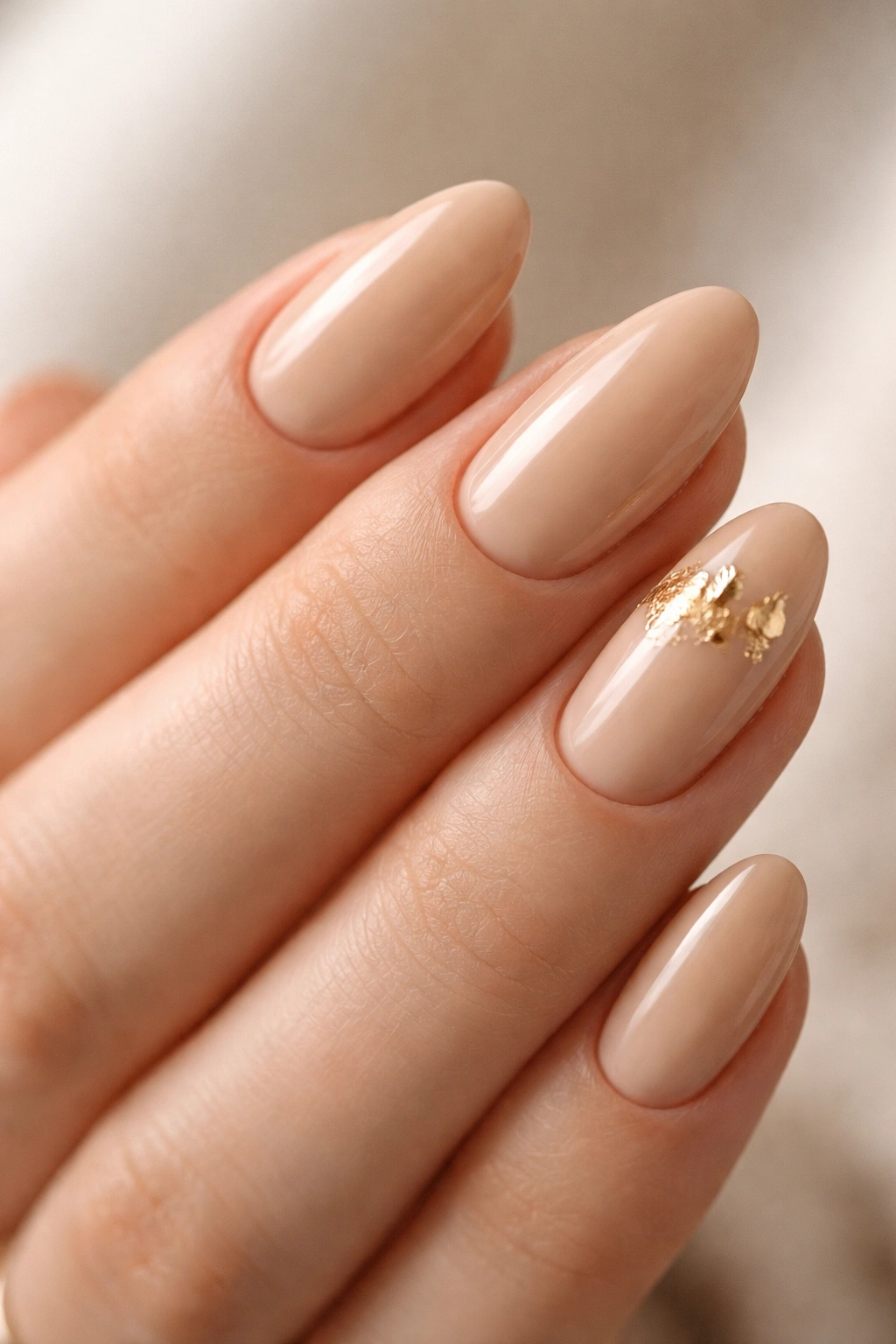 Close-up of beige almond nails with subtle gold foil accents near the cuticle