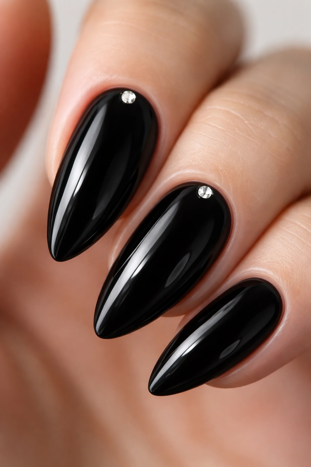 Close-up of black almond nail with a tiny rhinestone near the cuticle