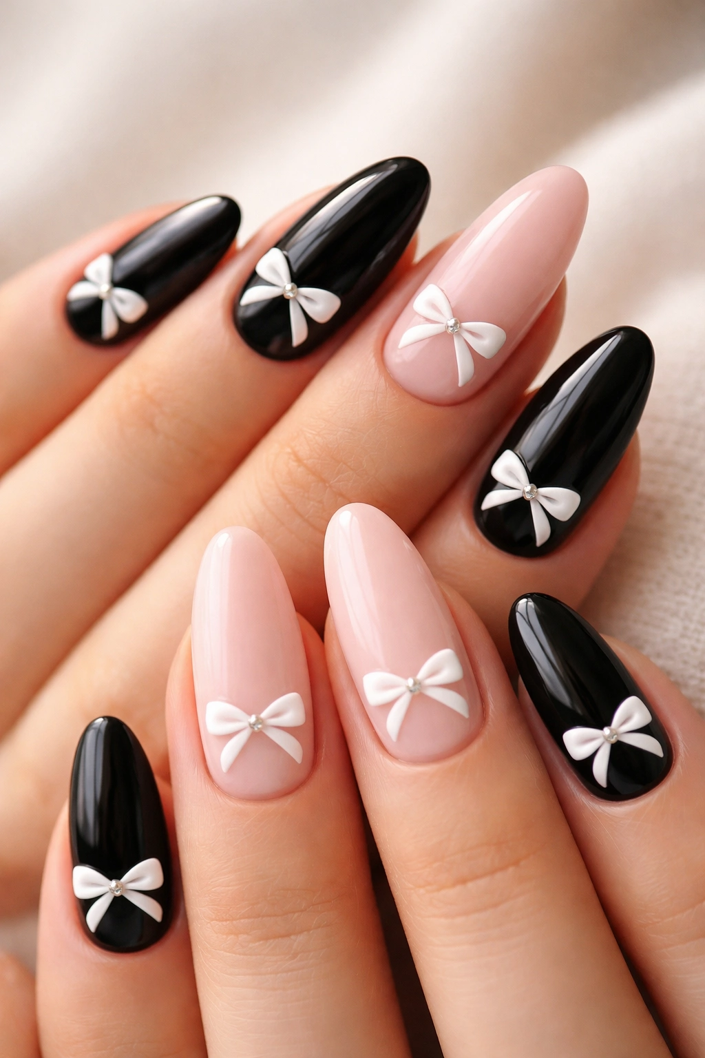 Black and blush almond nails with white bows on each nail in a crisp studio shot.