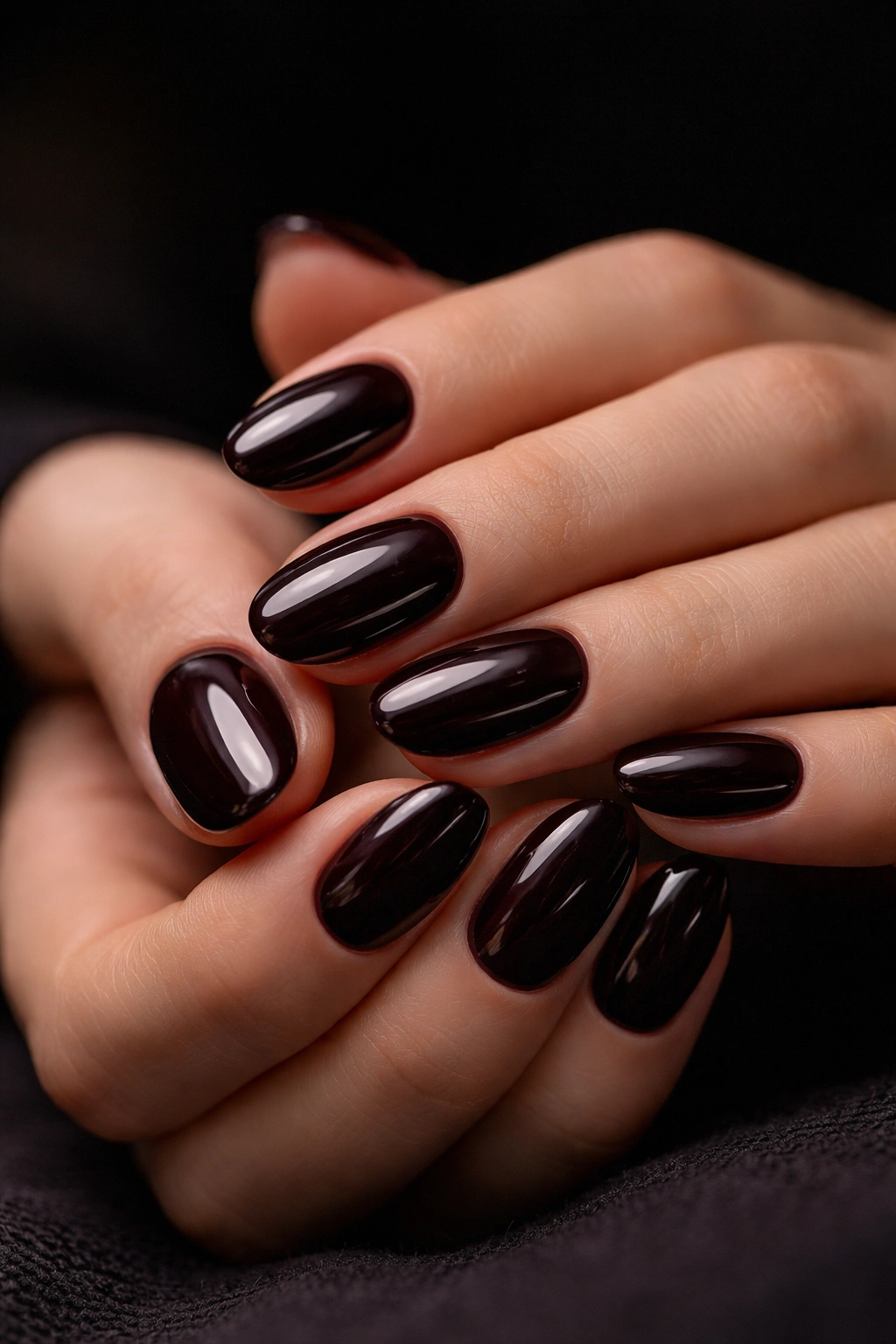 Close-up of short oval nails in deep black cherry sheen with glossy finish