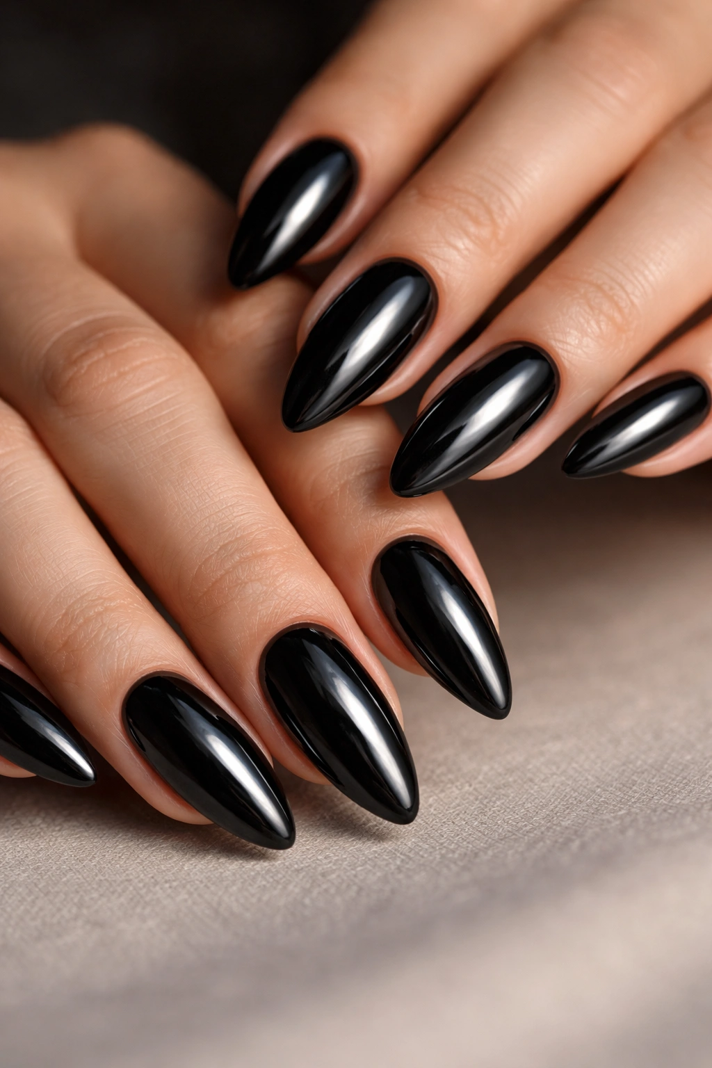 Close-up of black chrome almond nails on a neutral surface