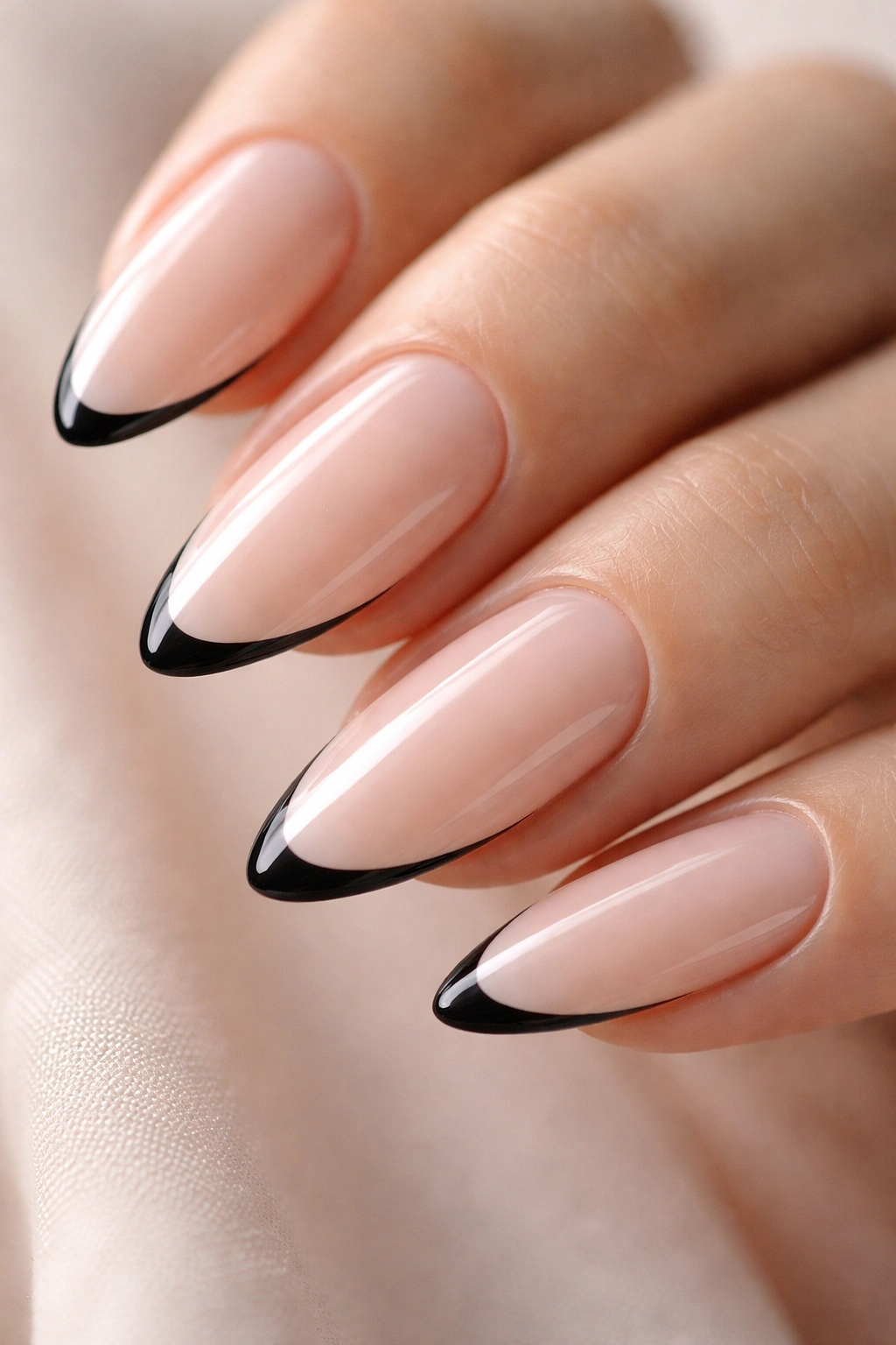 Close-up of almond fingernail with a thin black French tip on milky nude base.