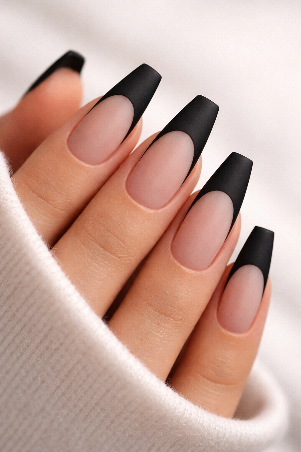 Close-up of coffin nails with matte black French tips over a sheer nude base