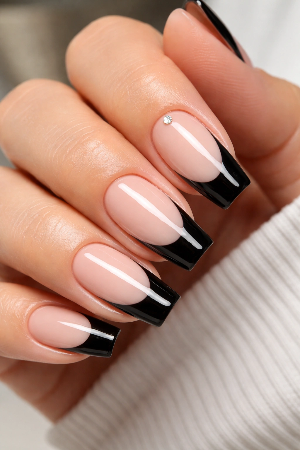Close-up of a black French tip manicure with a single tiny crystal near the cuticle on an accent nail.
