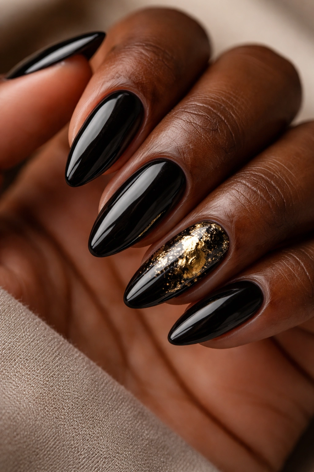 Black nails with gold foil accents on almond nails