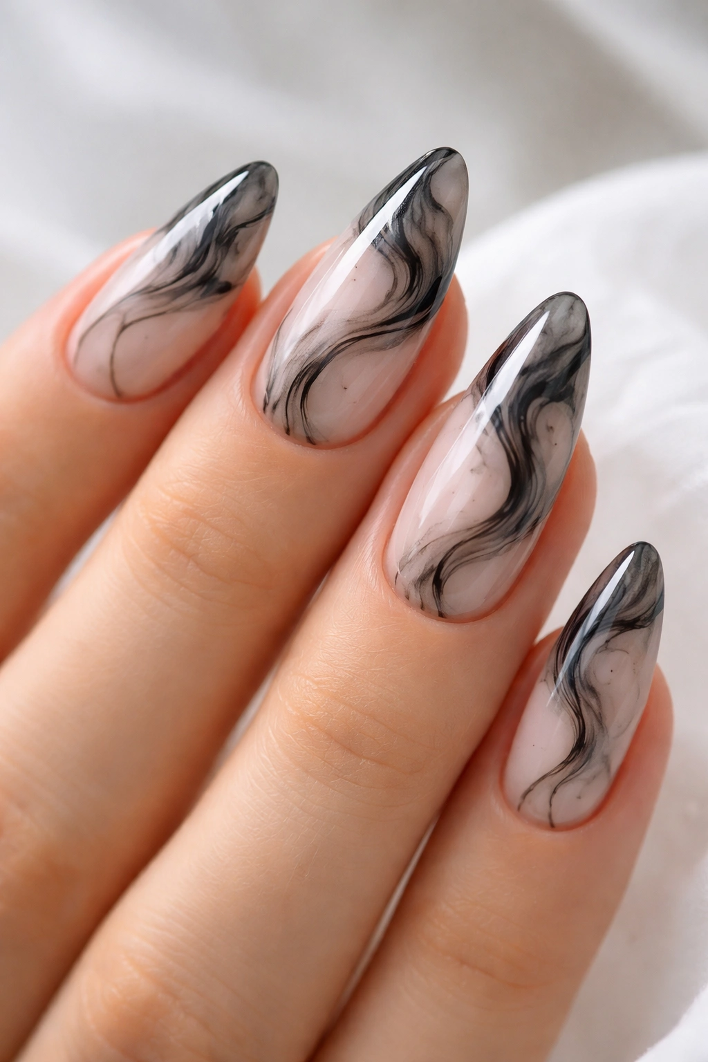 Close-up of black marble nail art with sheer base on almond nails