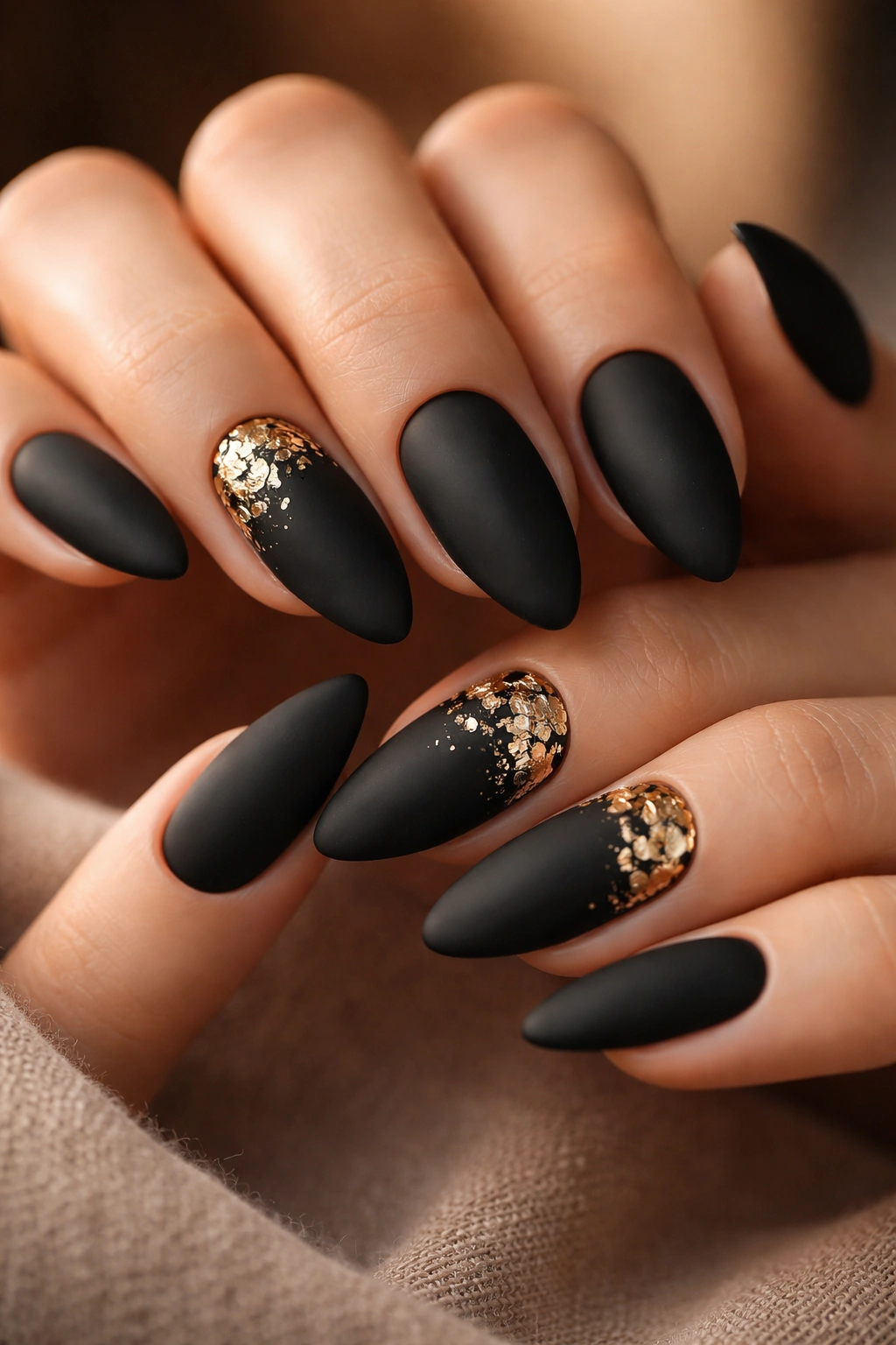 Close-up of almond nails with black polish and irregular gold foil flakes near the cuticle