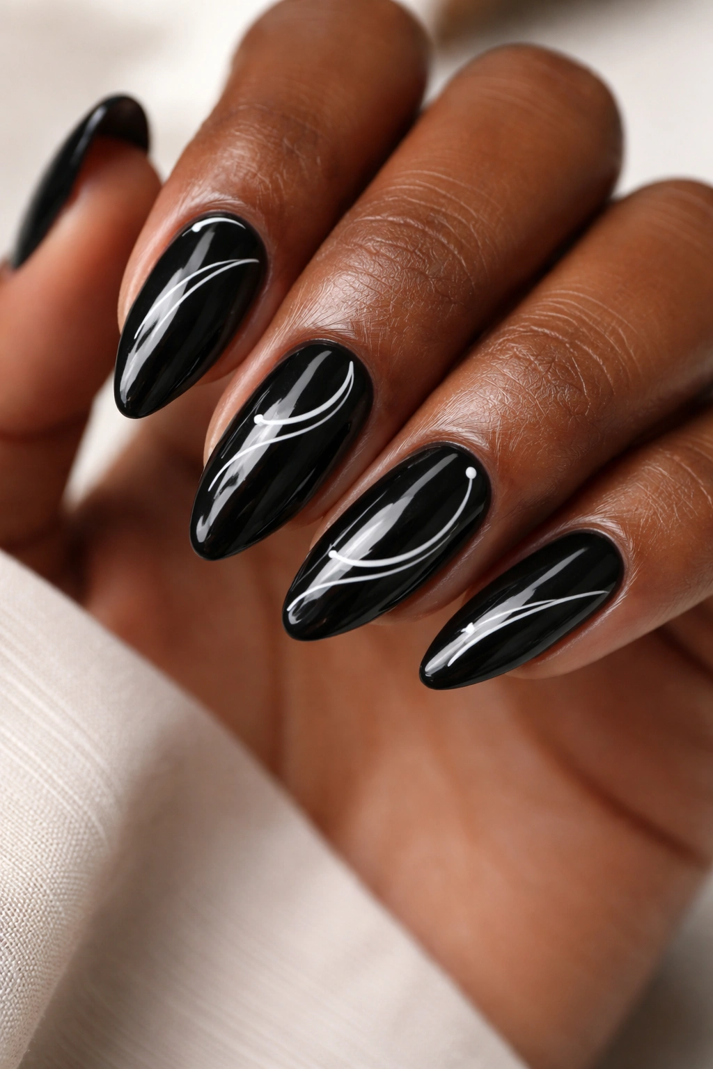 Close-up of black almond nails with thin white line art on a glossy finish