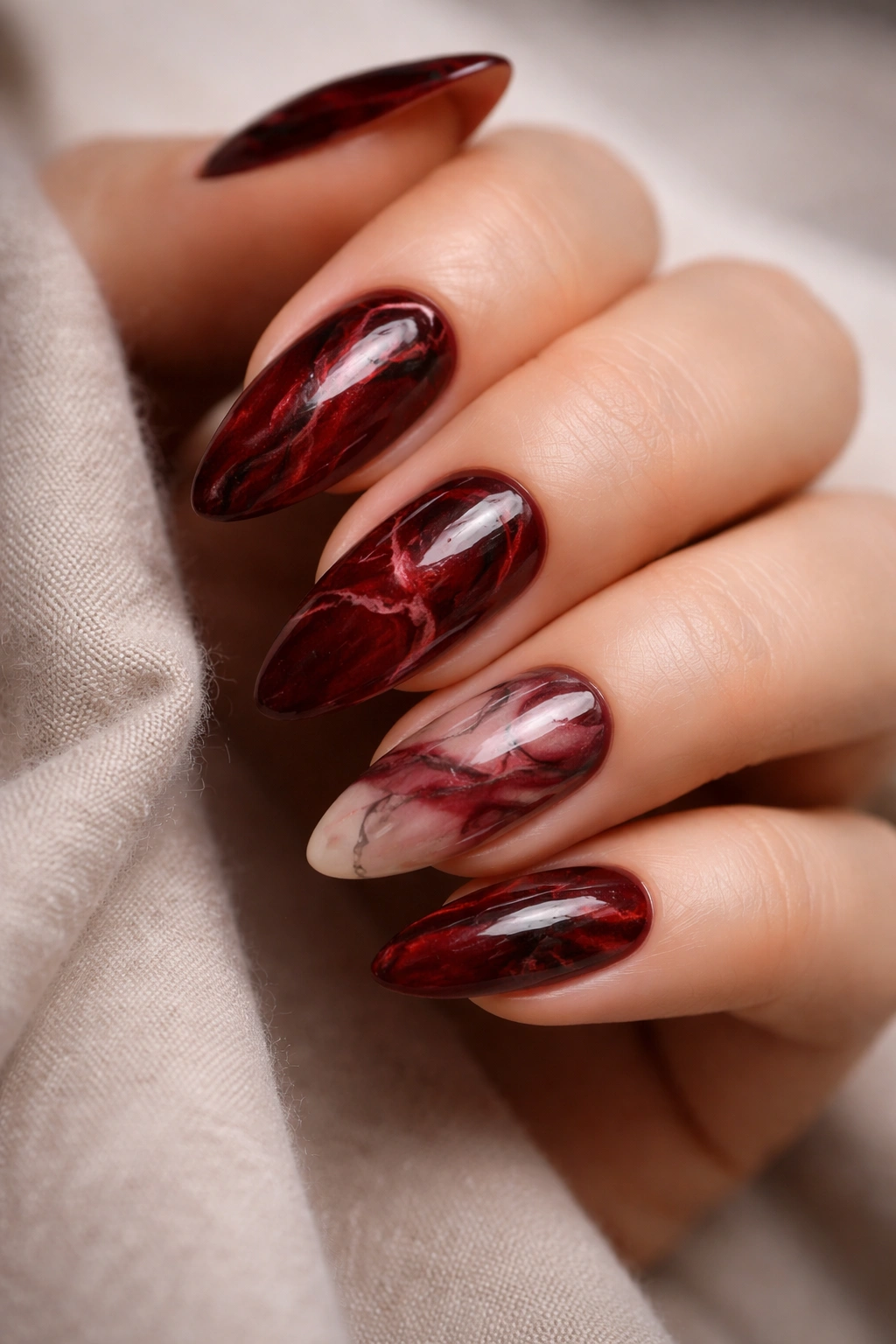Close-up of almond nails with deep red marble and fine black veining on a neutral background