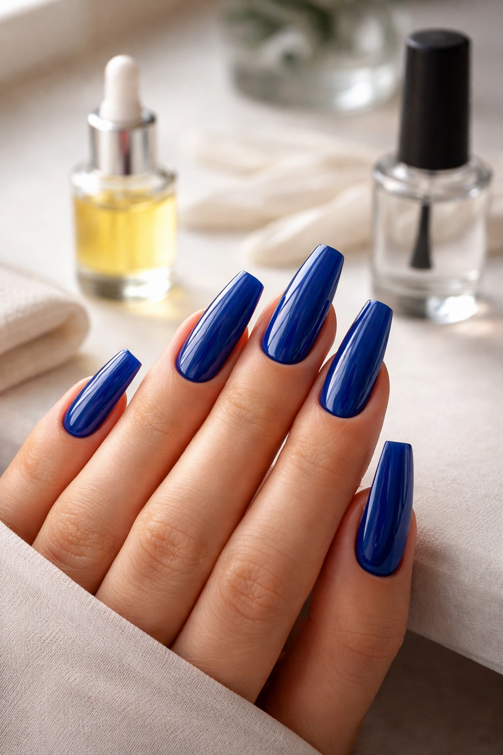 Close-up of glossy royal blue coffin nails on a hand with a neutral background