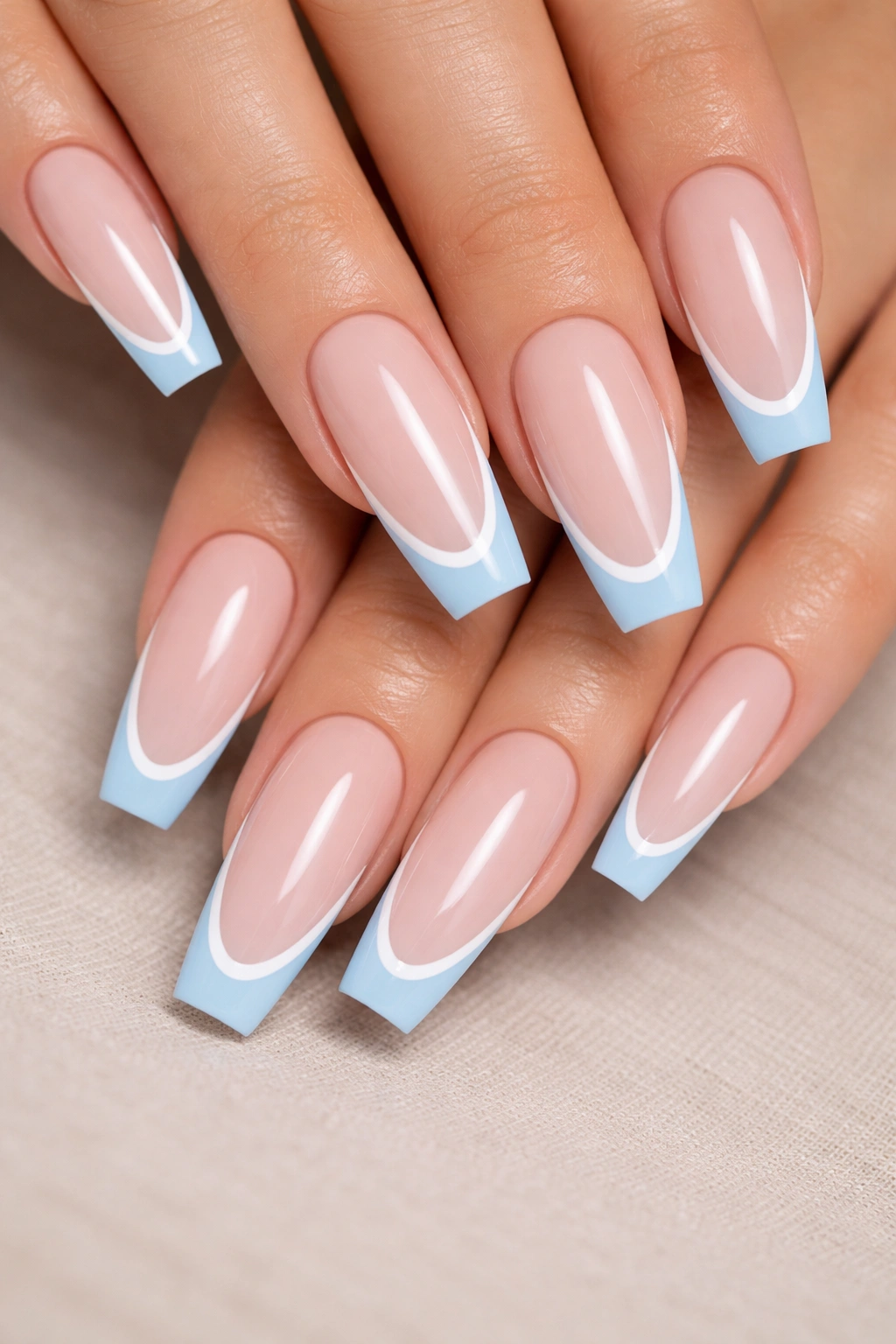 Close-up of coffin nails with light blue tips and a thin white outline on a cool nude base.