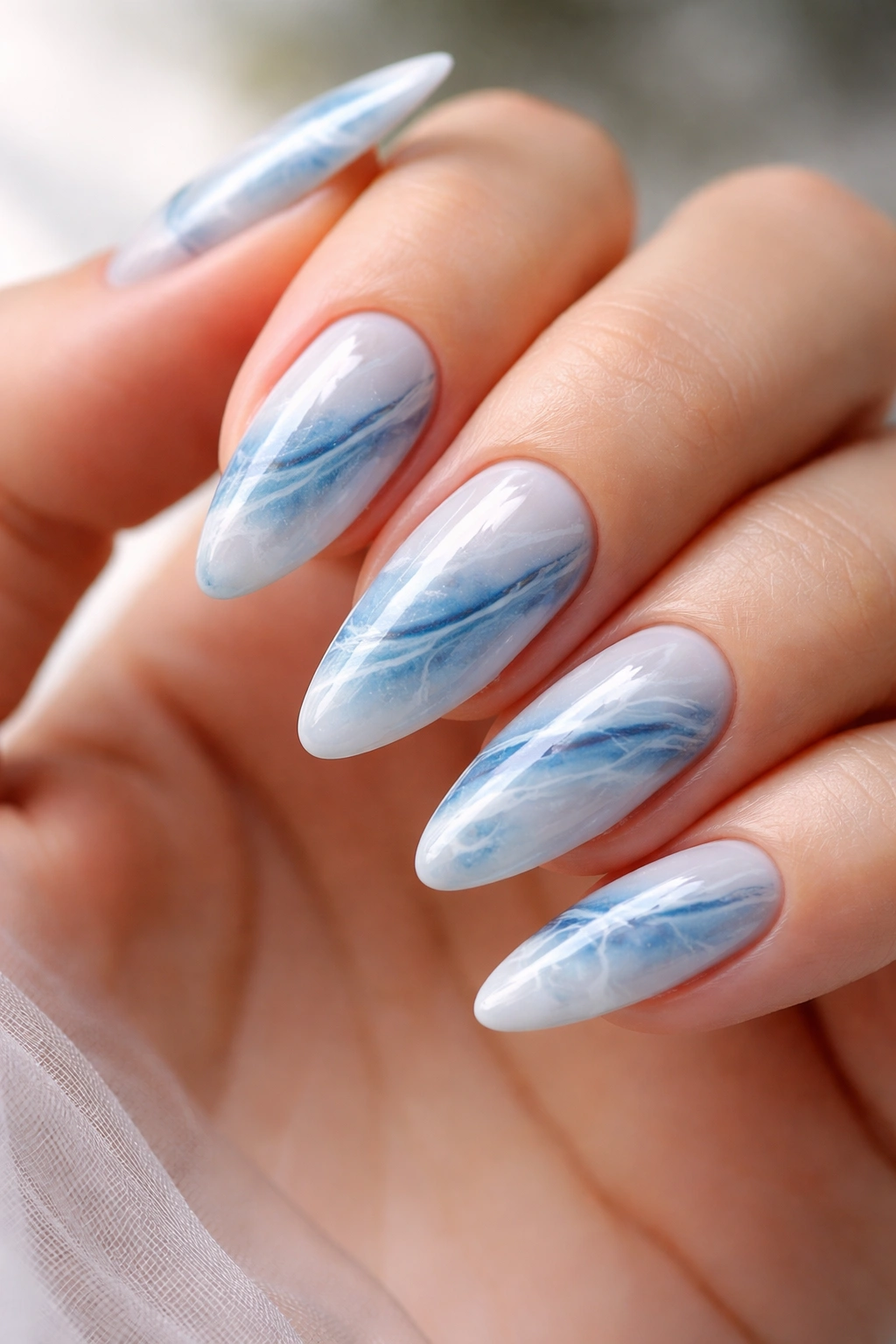 Blue marble almond nails with white veins on pale base