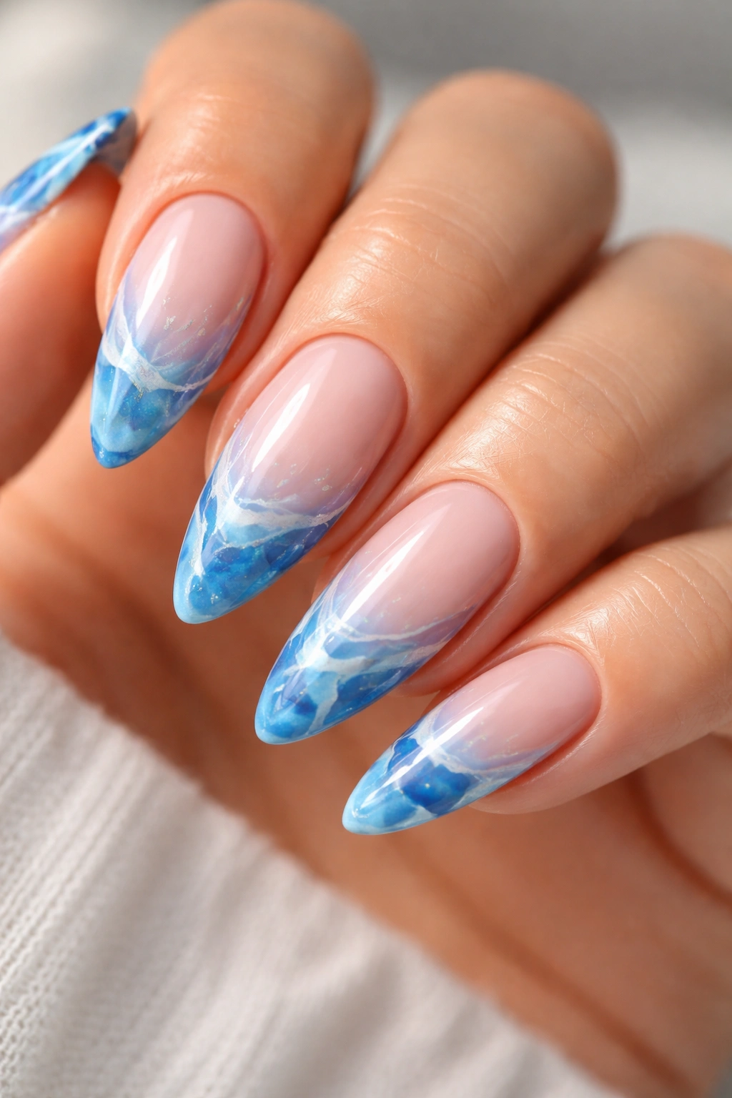 Almond nails with blue marble tip design on a pink base