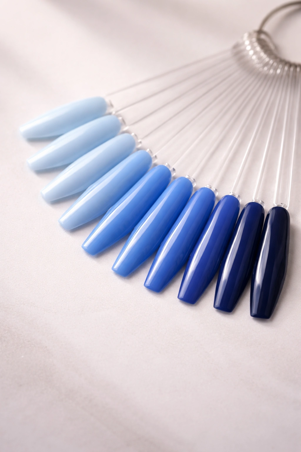 Row of blue nail polish swatches from light to dark on a neutral surface
