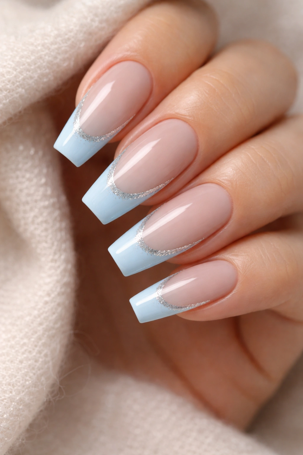 Close-up of coffin nails with light blue tips and a slim silver glitter border on nude base