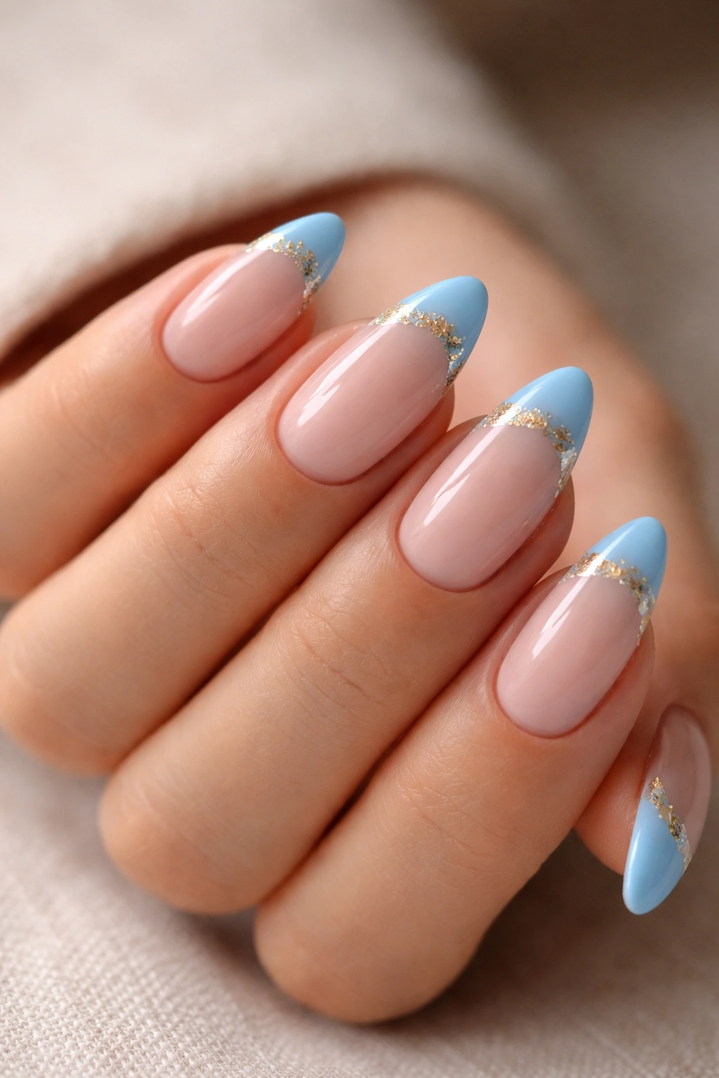 Blue French tips with gold foil accents on almond nails, close-up hand.