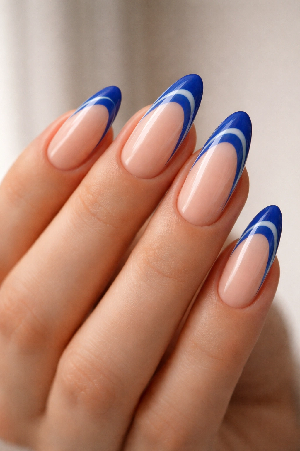 Close-up of almond nails with blue swirl tips on nude base, studio lighting